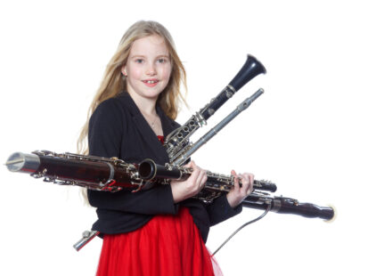 young blond girl holds woodwind instruments in studio against white background